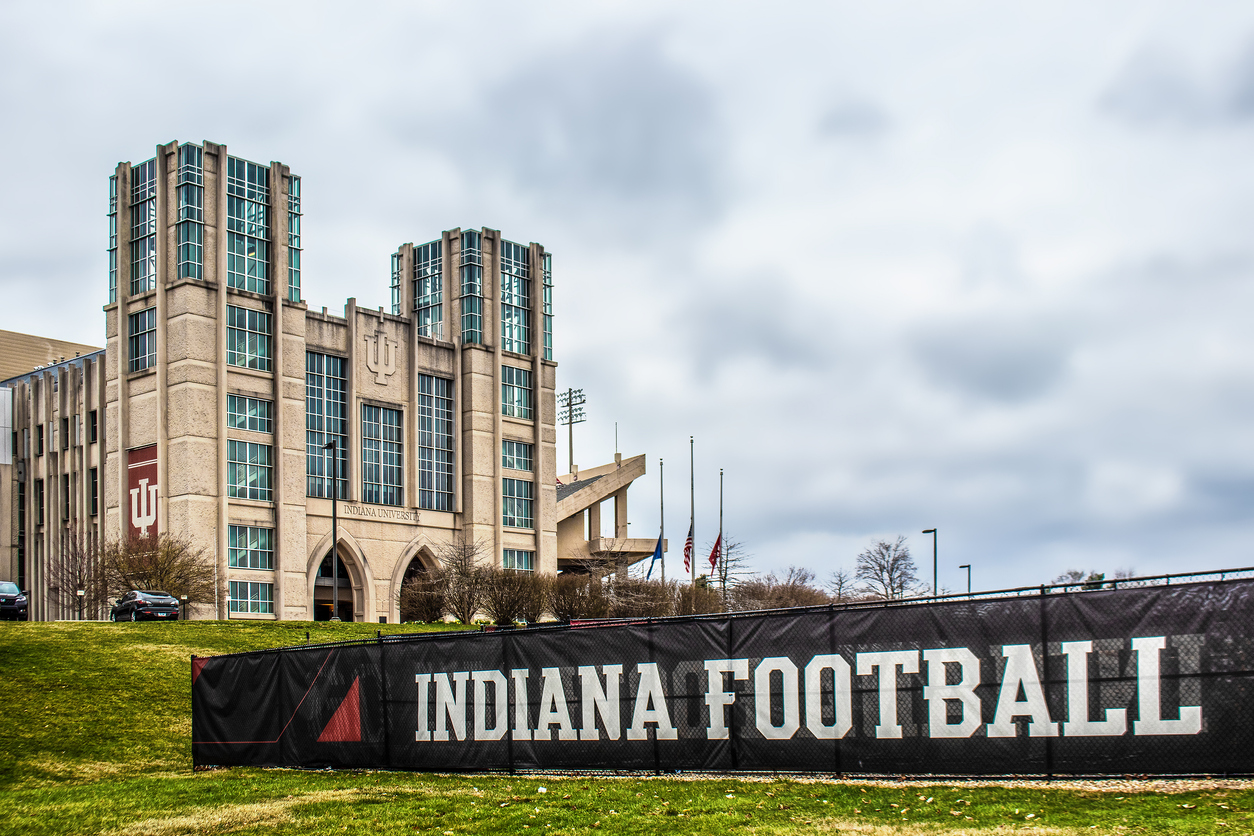 University of Indiana Hoosier stadium with flags at half mast under cloudy sky and sign Indiana Football in foreground